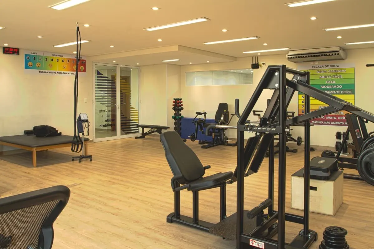 Vista ampla da sala com equipamentos de força e escala de esforço na parede