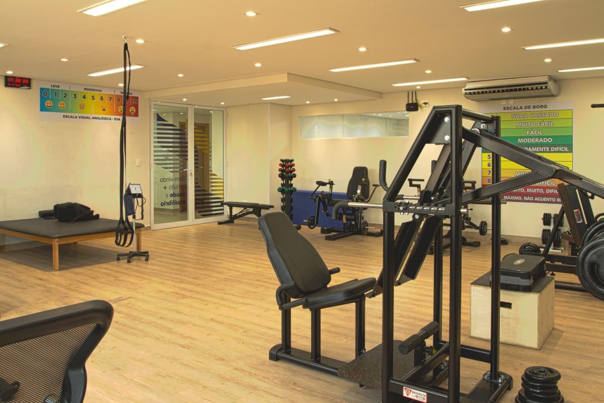 Vista ampla da sala com equipamentos de força e escala de esforço na parede